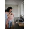Mushie Silicone Baby Bottle Brush in blush, shown in a kitchen setting with a mother holding her baby in a wrap.