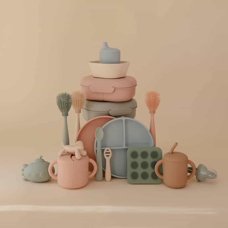 Mushie Silicone Baby Bottle Brush in blush, surrounded by various baby items in a soft, neutral setting.