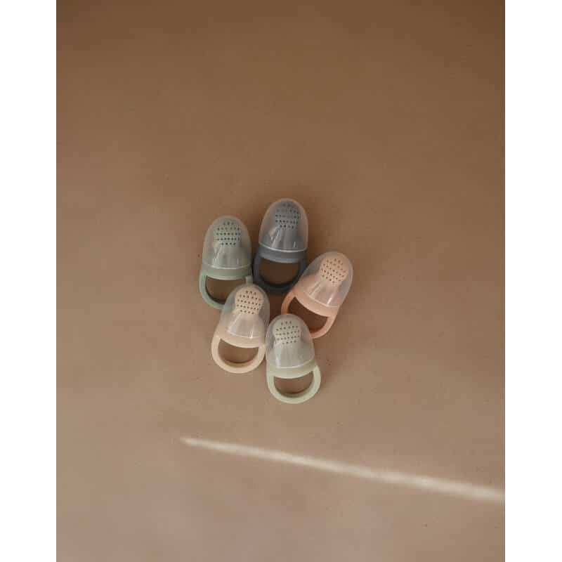 Mushie Silicone Fresh Food Feeders in blush, Cambridge blue, sage, and shifting sands arranged on a neutral background.