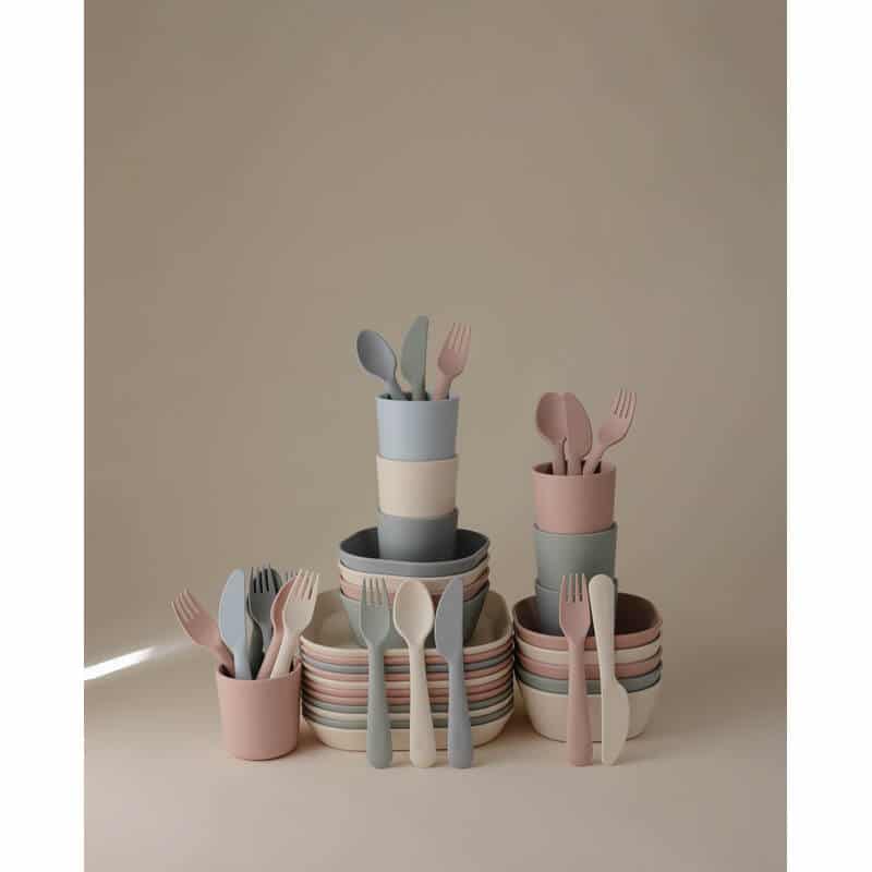 Mushie Dinnerware Cutlery Set in blush, cloud, dusty rose, and ivory, arranged in a stylish stack with bowls and cups.