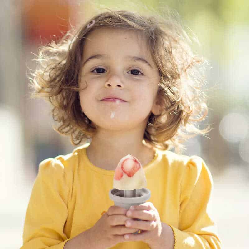 Haakaa Freeze-'n-Sip Ice Cream Mould Set in marigold, featuring a young girl enjoying a colorful ice pop outdoors.