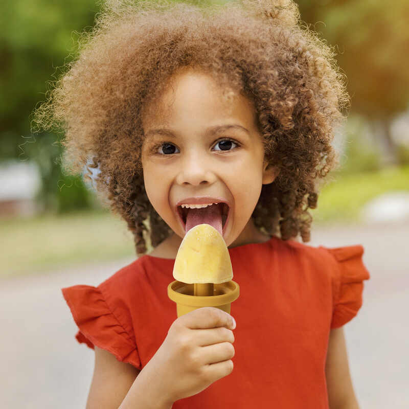 Haakaa Freeze-'n-Sip Ice Cream Mould Set in marigold, used by a smiling child enjoying a homemade ice cream treat outdoors.