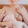 Haakaa Shell Wearable Silicone Breast Pump in use, discreetly worn under a nursing bra while breastfeeding a baby.