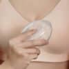 Haakaa Shell Wearable Silicone Breast Pump, clear, being held against a person's chest in a soft bra.