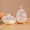 Haakaa Shell Wearable Silicone Breast Pump in clear silicone, showcasing two sizes on a wooden tray with decorative elements.
