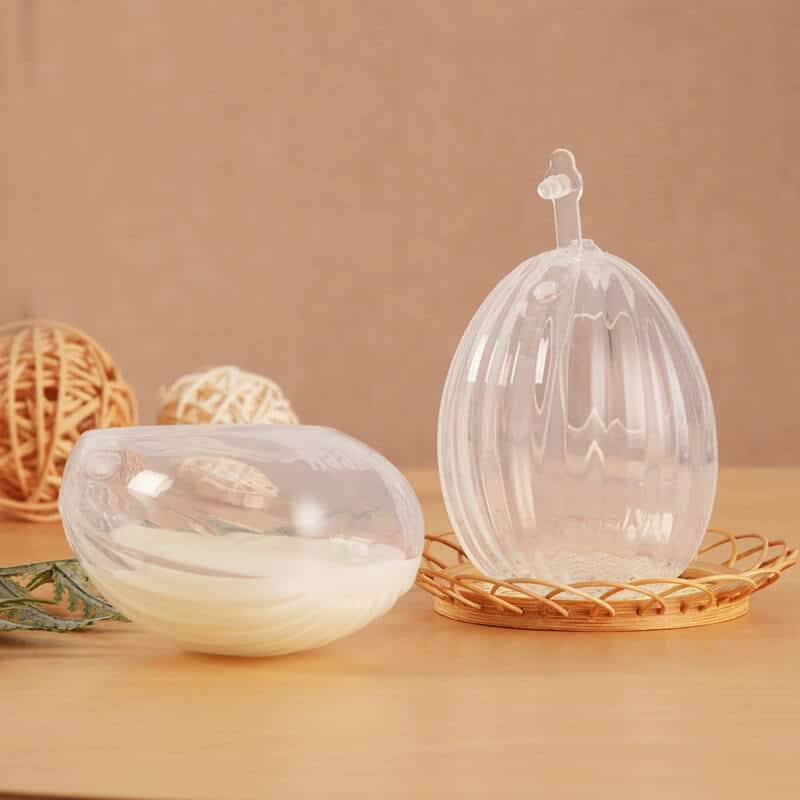 Haakaa Shell Wearable Silicone Breast Pump in clear silicone, showcasing two sizes on a wooden tray with decorative elements.