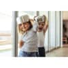 Two children playfully wearing stainless steel pots on their heads, smiling and having fun indoors.