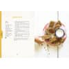Open cookbook page featuring granola bar recipe with a hand reaching for a bar and a glass of milk on a red plate.