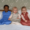 Maccie Winter Sleep Sack TOG 2 in berry pink, cobalt blue, and oatmeal beige, worn by three children on a bed.