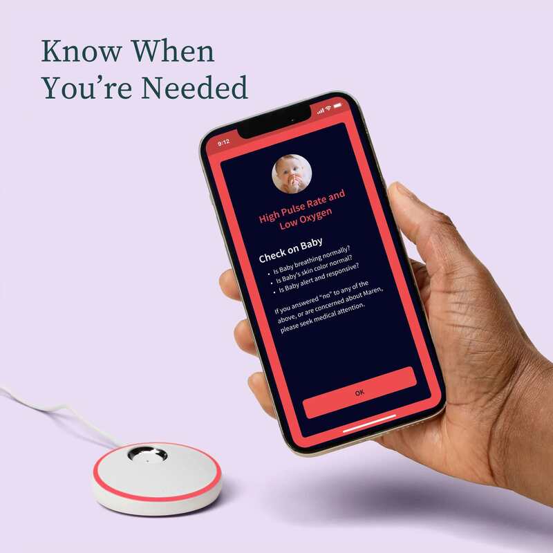 Owlet Dream Sock with smartphone app displaying baby’s health metrics, featuring a hand holding the phone.