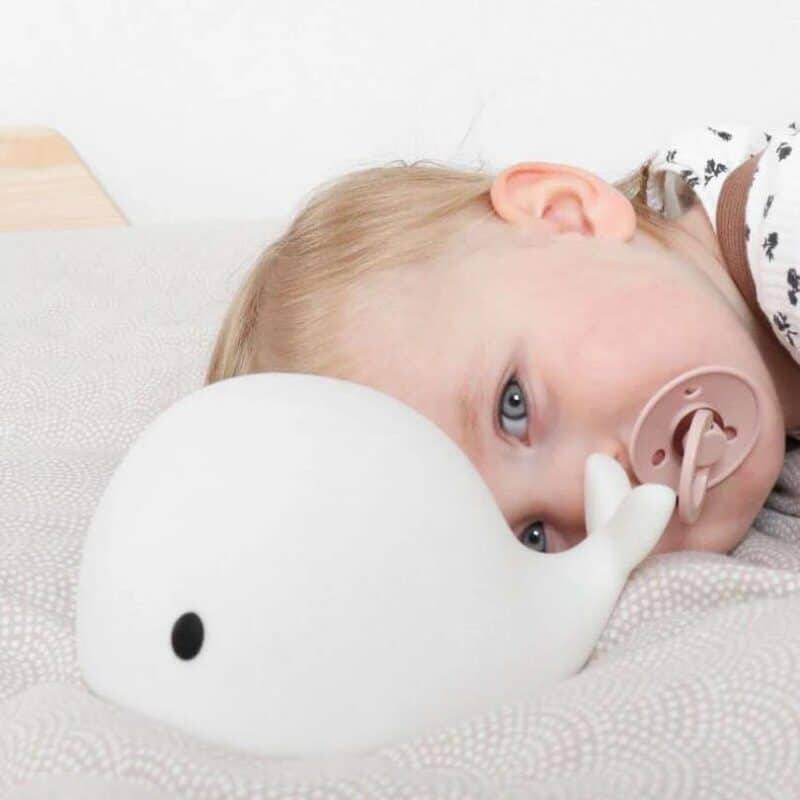 Flow Amsterdam Night Light featuring Liva the whale, soft white design, with a child resting beside it in a cozy bedroom