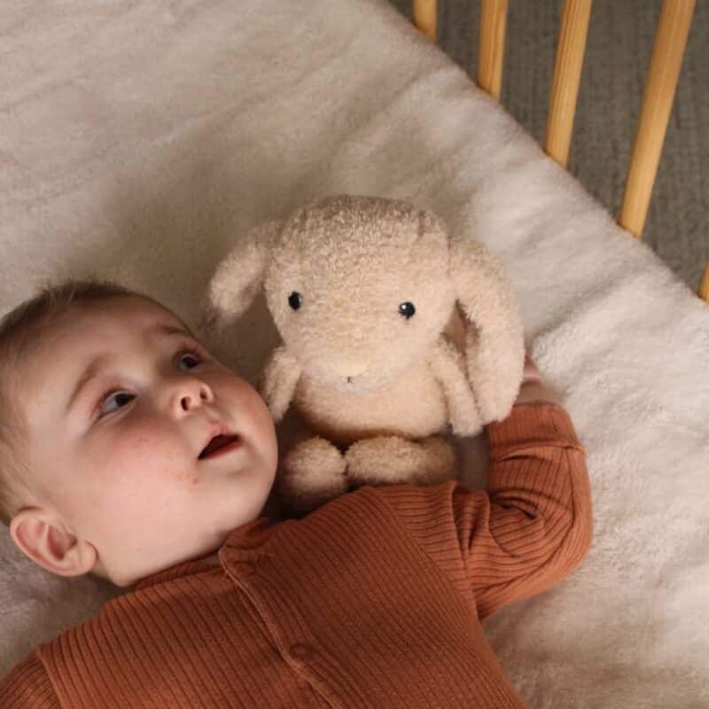 Flow Amsterdam Plush Night Light featuring Liva the bunny, soft beige color, beside a baby in a cozy crib setting.