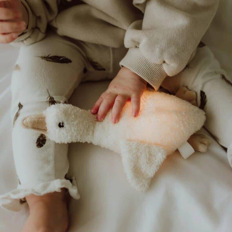 Flow Amsterdam Plush Night Light in the shape of Liva, a soft white goose, gently glowing in a child's hands.