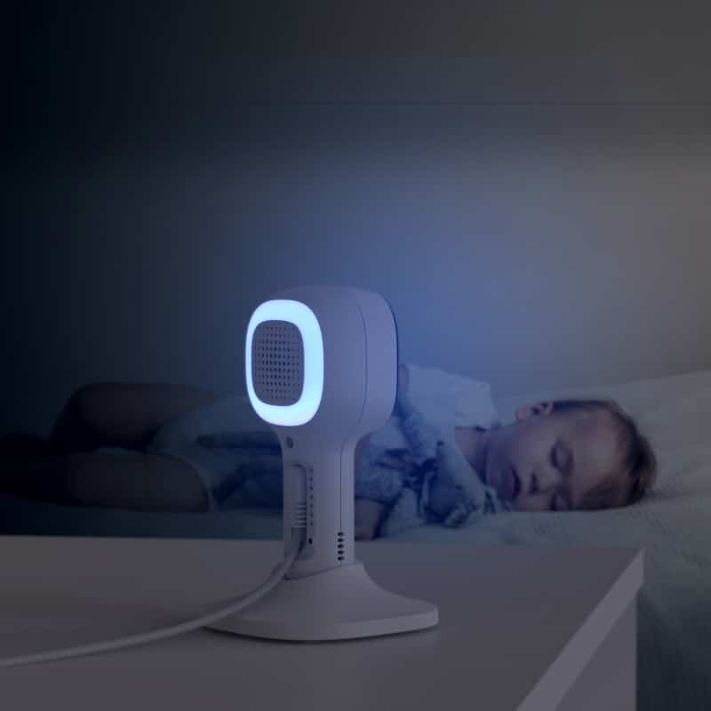 Hubble Nursery Pal Cloud in white, projecting a soft blue light beside a sleeping baby in a dimly lit room.