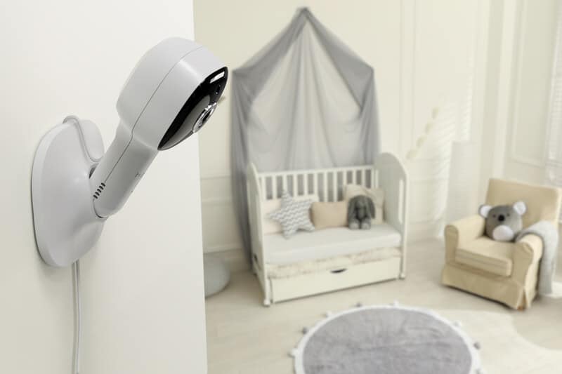 Hubble Nursery Pal Cloud monitor mounted on wall, overlooking a cozy nursery with a crib and plush toys.