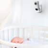 Hubble Nursery Pal Dual Vision baby monitor mounted on a wall, overlooking a sleeping infant in a crib.