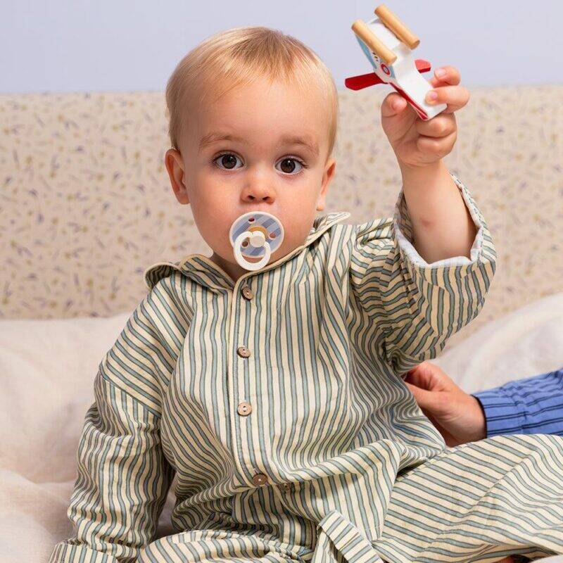 BIBS Studio Colour Pacifier 2 Pack in Baby Blue Dusty Blue Mix and Jasmine Fossil Grey Mix, held by a child in pajamas.