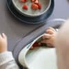 Difrax LOVI Silicone Bib in nude and pistachio, shown with a child reaching for strawberries on a table.