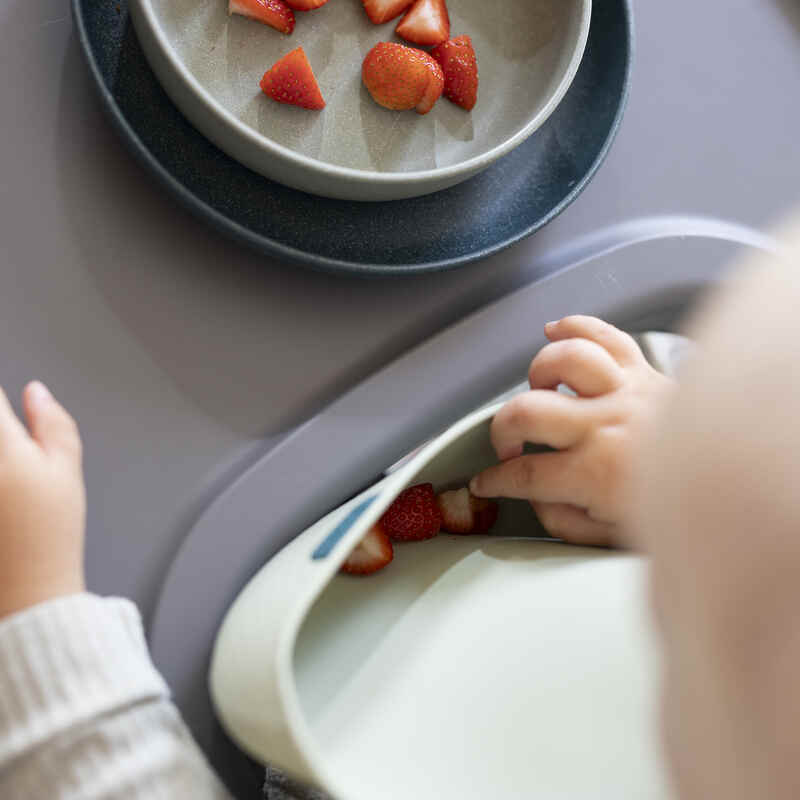 Difrax LOVI Silicone Bib in nude and pistachio, shown with a child reaching for strawberries on a table.