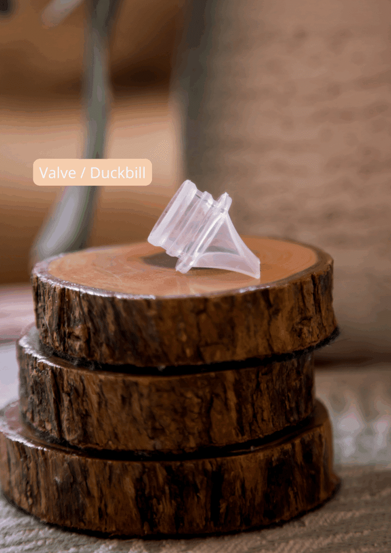 Mommy Material Milk it Silicone Valve in clear, positioned on stacked wooden slices, showcasing its unique duckbill design.