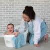 Shnuggle Bamboo Wearable Baby Towel in blue, featuring a smiling baby in a bath with a parent nearby.