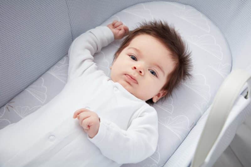 Shnuggle Dreami Moses Basket fitted sheets in grey, featuring a soft design, with a baby lying comfortably on one.