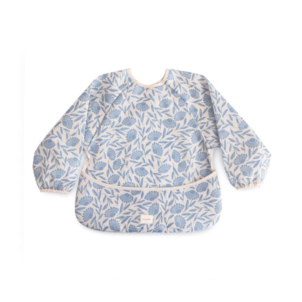 Mushie Long Sleeve Bib in blue flowers design, featuring elastic cuffs and a front pocket for easy cleanup.
