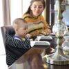 Momcozy Mtwml Portable High Chair in black with geometric design, featuring a child seated at a dining table with an adult.