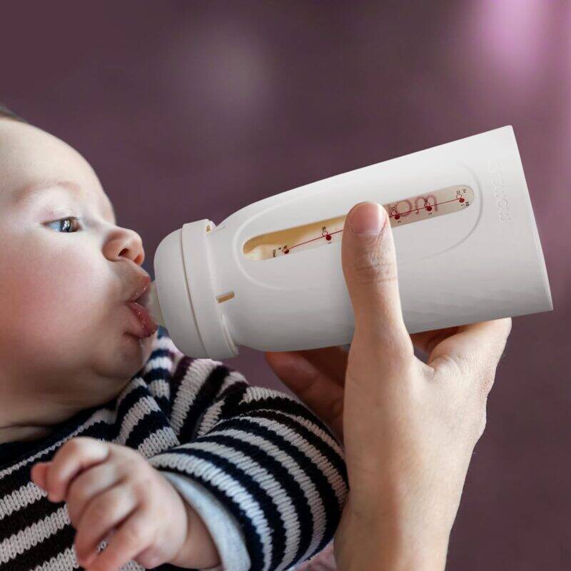 Momcozy Disposable Baby Bottle Kit in white, held by a caregiver while a baby drinks from it, featuring a clear measurement