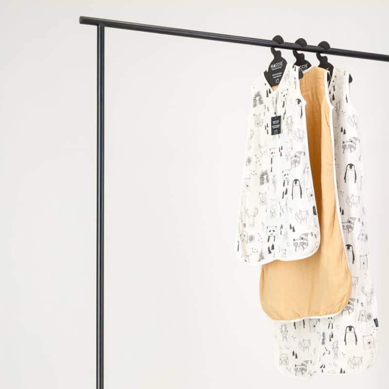 Maccie Summer Sleep Sac for 3-9 months in beige with scandi animals, hanging on a black rack with two other designs.