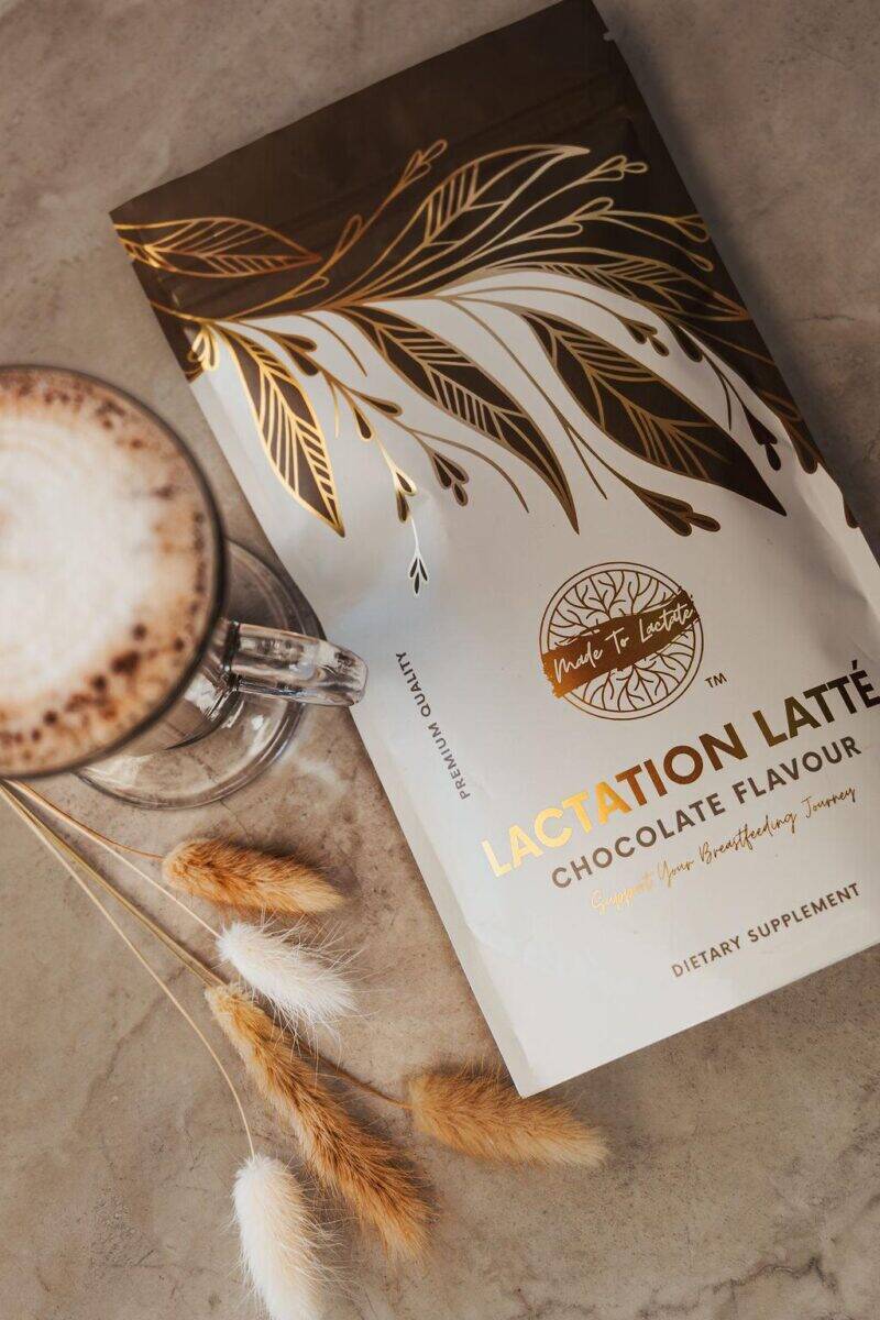Made to Lactate Lactation Chocolate Latté package beside a glass of latte, featuring a stylish design with gold accents.