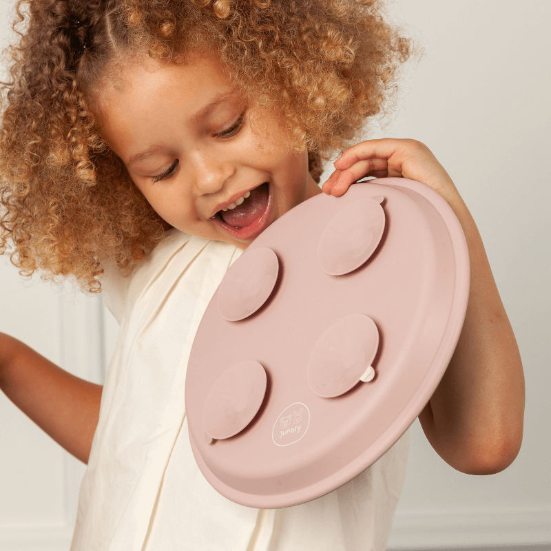 Junary Little Gripper Starter Kit in soft pink, held by a smiling child, showcasing its suction feature for easy feeding.