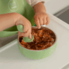 Junary Little Bites Bowl Duo in green, featuring a child using a matching spoon to eat from the bowl.