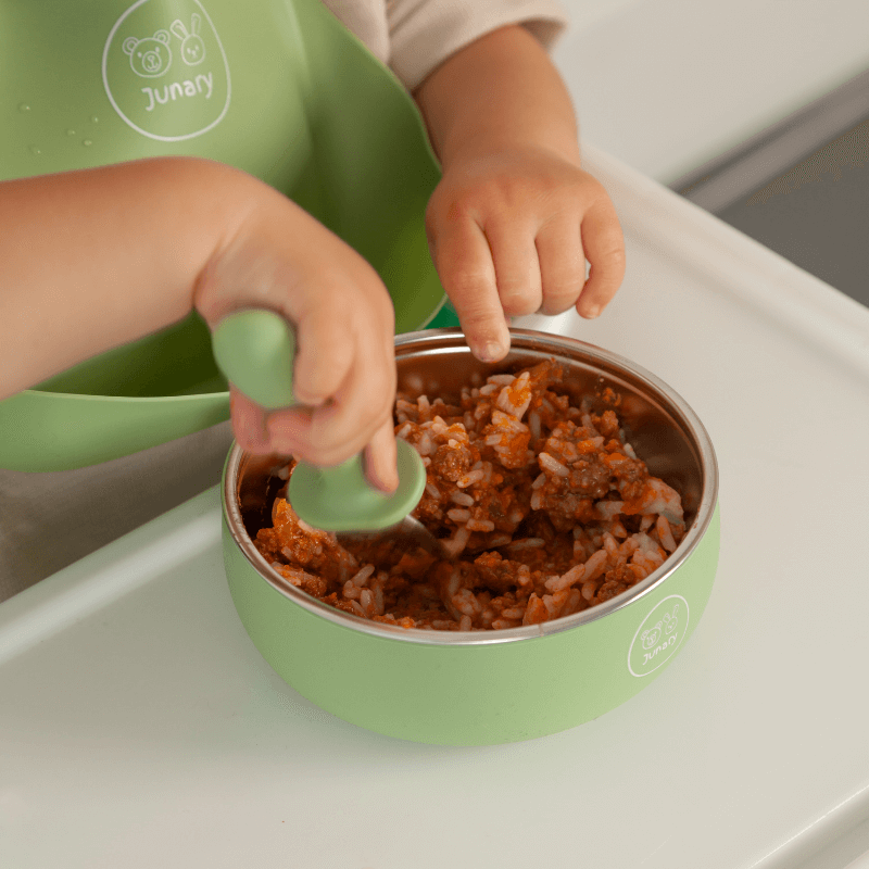 Junary Little Bites Bowl Duo in green, featuring a child using a matching spoon to eat from the bowl.