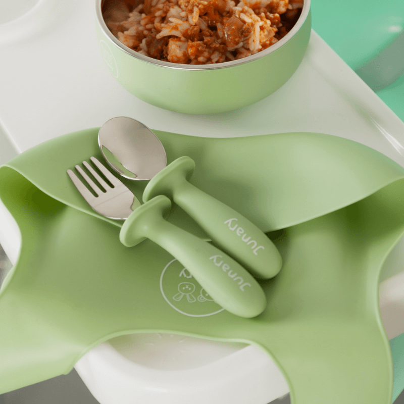 Junary Little Bites Cutlery Duo in soft green, featuring a fork and spoon with ergonomic handles, set on a silicone mat.