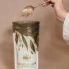 Made to Lactate Lactation Chocolate Latté in a gold and white pouch, with a hand pouring powder using a spoon.