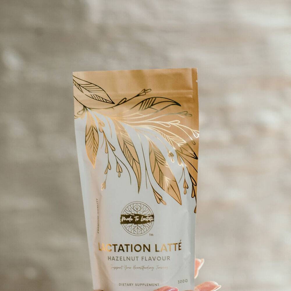 Made to Lactate Hazelnut Latté in a decorative pouch, held in a hand against a soft, neutral background.