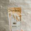 Made to Lactate Hazelnut Latté in a decorative pouch, held in a hand against a soft, neutral background.