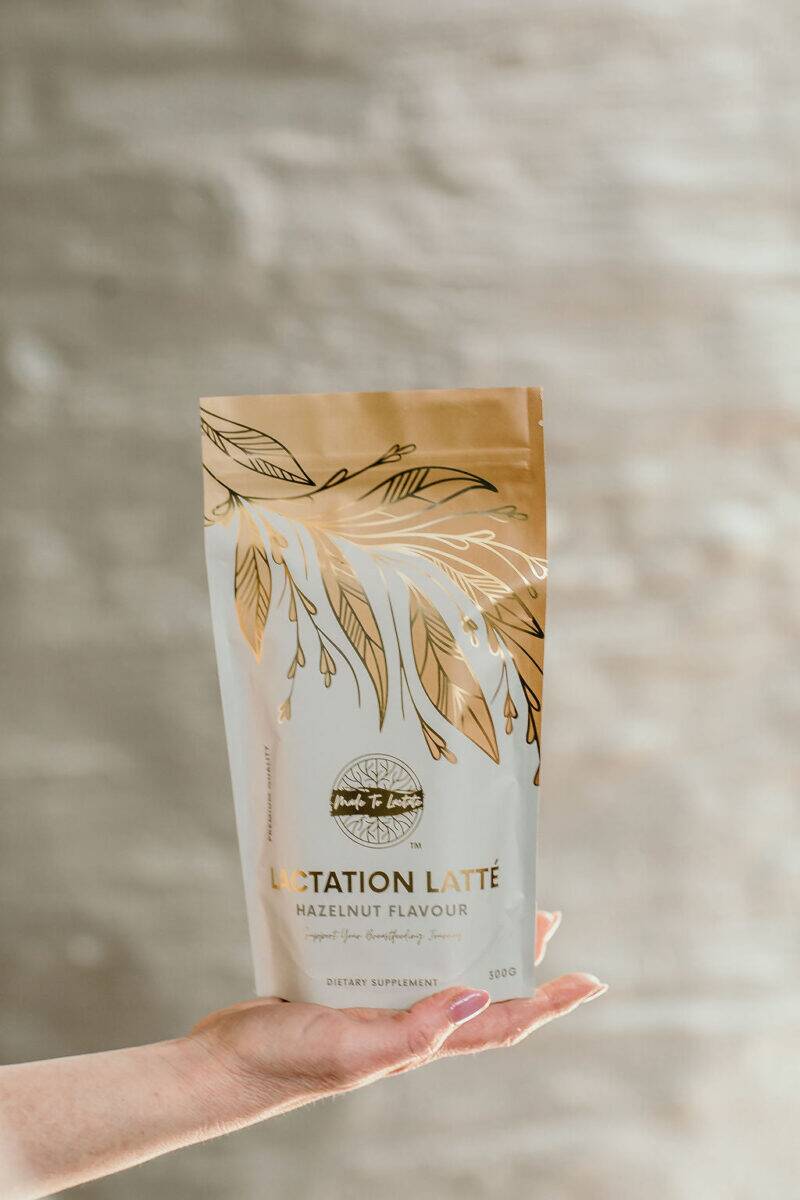 Made to Lactate Hazelnut Latté in a decorative pouch, held in a hand against a soft, neutral background.