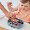 b.box silicone plate in Ocean color with divided sections, being used by a toddler in a high chair, featuring snacks.