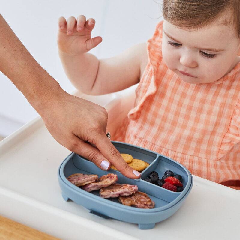 b.box silicone plate in Ocean color with divided sections, being used by a toddler in a high chair, featuring snacks.