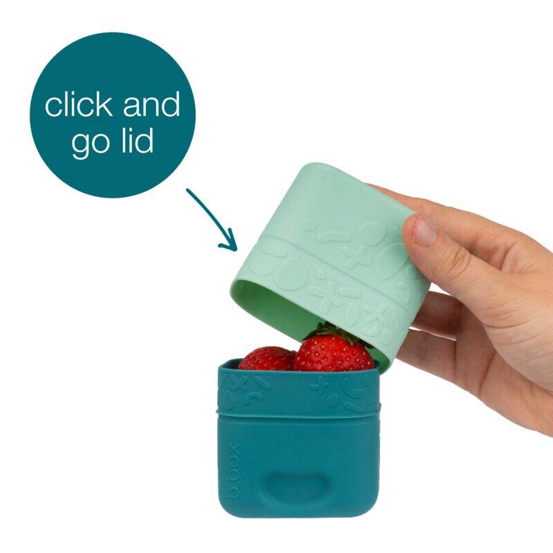 b.box silicone snack cup in forest green with a click-and-go lid, holding strawberries, being held by a hand.