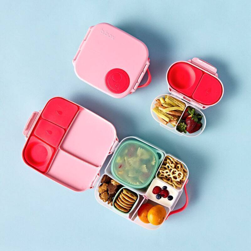 b.box snackbox in flamingo fizz with multiple compartments, featuring snacks and fruits, set against a light blue background.