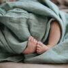 Mushie Swaddle in soft green, featuring a cozy baby wrapped up with tiny feet peeking out.
