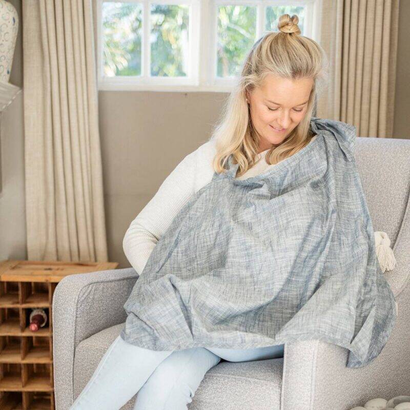 Baby Sense denim nursing cover draped over a mother while seated in a cozy chair, providing privacy and comfort.