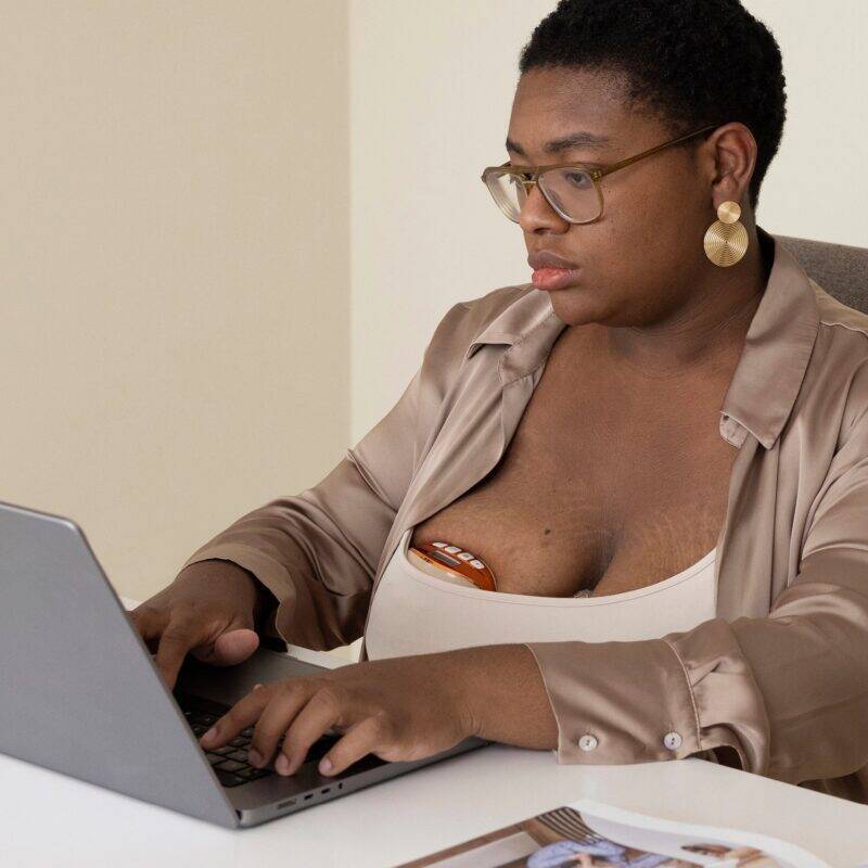 Difrax Handsfree Breastpump in use, worn discreetly under clothing while a woman works on a laptop at a desk.