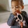 Difrax Crown Teething Ring in soft pink and white, held by a baby, designed to soothe teething discomfort.