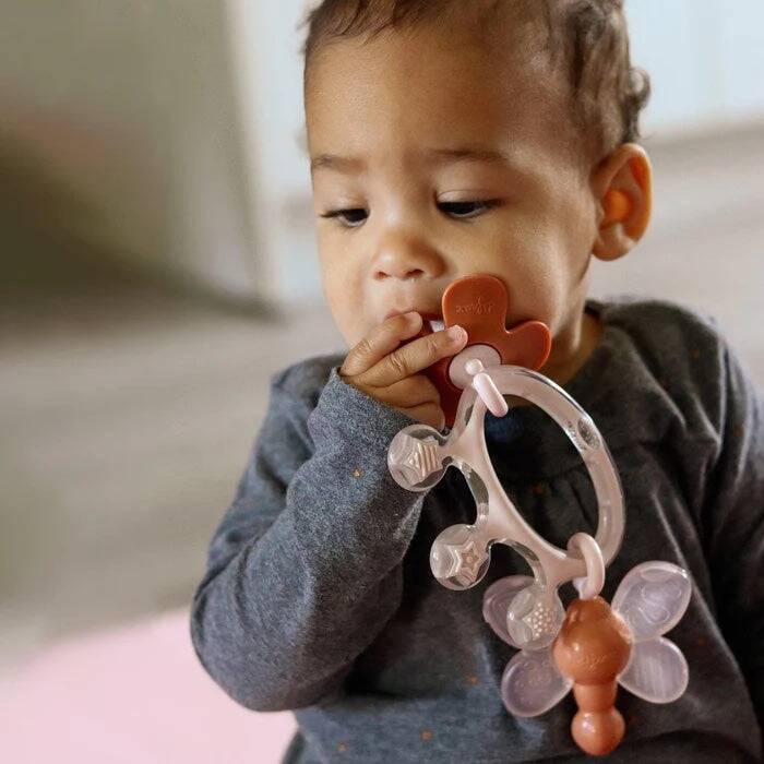 Difrax Crown Teething Ring in soft pink and white, held by a baby, designed to soothe teething discomfort.