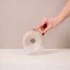 Difrax Handsfree Breastpump in clear with a soft pink accent, shown from the front with a hand holding it.