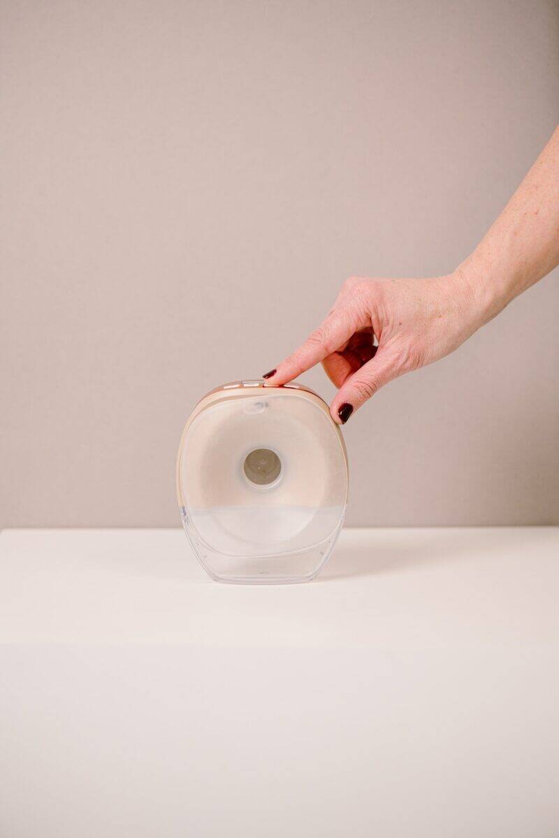 Difrax Handsfree Breastpump in clear with a soft pink accent, shown from the front with a hand holding it.